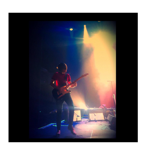 Musiker spelar gitarr på scen med färgglad belysning.