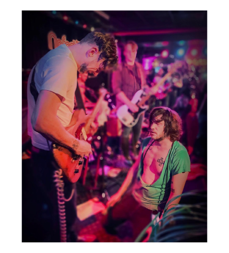 En musikgrupp uppträder på en scen, med fokus på en gitarrist och en åskådare.