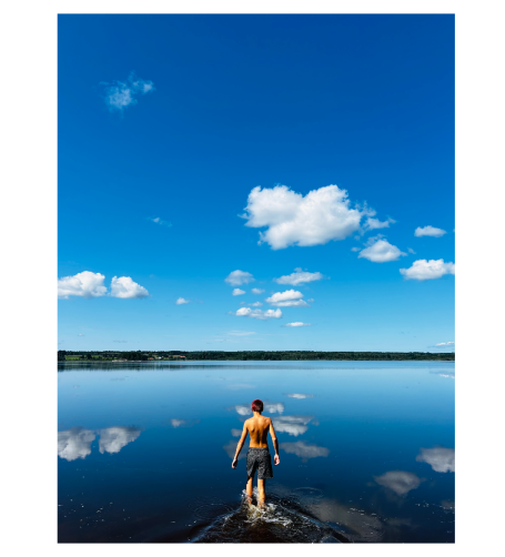 En person går ut på en spegelblanka sjö under en klarblå himmel med vita moln.